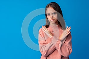 Young beautiful teen girl crossing arms doing negative sign on blue background