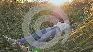 A young beautiful teen girl falls into a wheat field on a soft sunset.