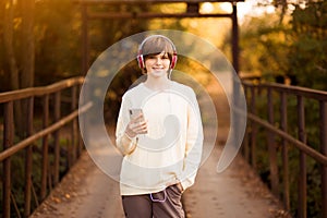 Young beautiful teen girl in headphones listening to music in phone while walk by street at autumn