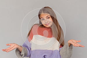 Young beautiful teen girl making shrugging shoulders isolated on grey background