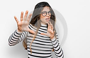Young beautiful teen girl wearing casual clothes and glasses afraid and terrified with fear expression stop gesture with hands,