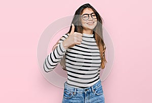 Young beautiful teen girl wearing casual clothes and glasses doing happy thumbs up gesture with hand