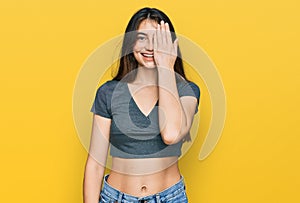 Young beautiful teen girl wearing casual crop top t shirt covering one eye with hand, confident smile on face and surprise emotion