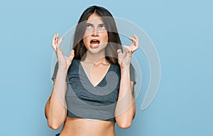 Young beautiful teen girl wearing casual crop top t shirt crazy and mad shouting and yelling with aggressive expression and arms