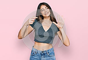 Young beautiful teen girl wearing casual crop top t shirt showing and pointing up with fingers number seven while smiling