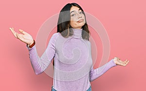 Young beautiful teen girl wearing turtleneck sweater clueless and confused expression with arms and hands raised