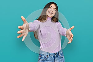 Young beautiful teen girl wearing turtleneck sweater looking at the camera smiling with open arms for hug