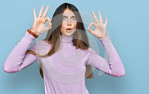 Young beautiful teen girl wearing turtleneck sweater looking surprised and shocked doing ok approval symbol with fingers