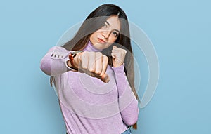 Young beautiful teen girl wearing turtleneck sweater punching fist to fight, aggressive and angry attack, threat and violence