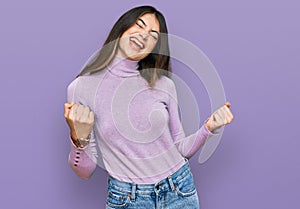 Young beautiful teen girl wearing turtleneck sweater very happy and excited doing winner gesture with arms raised, smiling and