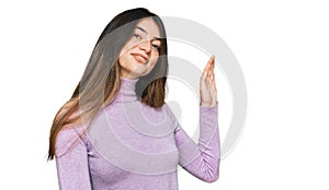 Young beautiful teen girl wearing turtleneck sweater waiving saying hello happy and smiling, friendly welcome gesture