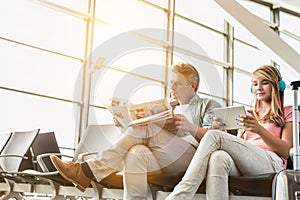 Young beautiful teenage girl watching movie on digital tablet with headphones on while her father is reading newspaper in airport