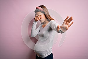 Young beautiful teenager girl pregnant expecting baby over isolated pink background covering eyes with hands and doing stop