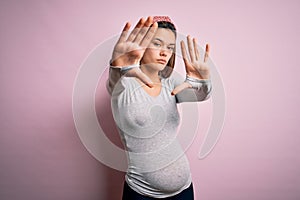 Young beautiful teenager girl pregnant expecting baby over isolated pink background doing frame using hands palms and fingers,