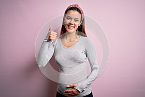 Young beautiful teenager girl pregnant expecting baby over isolated pink background doing happy thumbs up gesture with hand
