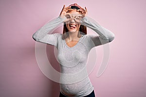Young beautiful teenager girl pregnant expecting baby over isolated pink background doing ok gesture like binoculars sticking
