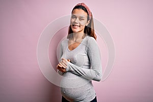Young beautiful teenager girl pregnant expecting baby over isolated pink background with hands together and crossed fingers