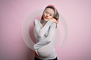 Young beautiful teenager girl pregnant expecting baby over isolated pink background Hugging oneself happy and positive, smiling