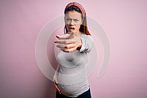 Young beautiful teenager girl pregnant expecting baby over isolated pink background pointing displeased and frustrated to the