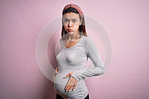 Young beautiful teenager girl pregnant expecting baby over isolated pink background puffing cheeks with funny face