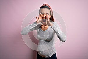Young beautiful teenager girl pregnant expecting baby over isolated pink background Shouting angry out loud with hands over mouth