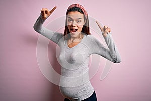 Young beautiful teenager girl pregnant expecting baby over isolated pink background smiling amazed and surprised and pointing up