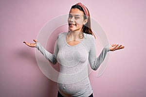 Young beautiful teenager girl pregnant expecting baby over isolated pink background smiling showing both hands open palms,