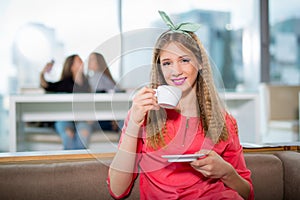 Young beautiful teenager girl sitting in cafe with a white cup,