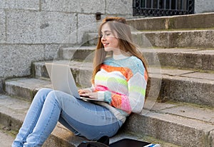 Young beautiful teenager student girl working and studying on laptop in a european city outdoors