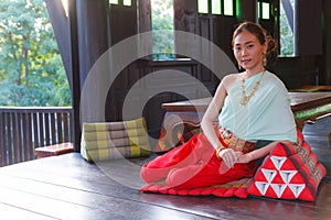 Young Beautiful Thai Asian woman dressing vintage Traditional Thai costume sits on triangle cushion at balcony. Thailand Cultural