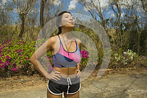 Young beautiful tired and breathless runner Asian woman exhausted and sweaty after hard running workout at trail road park in