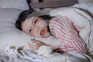 Young beautiful tired and ill Asian Japanese woman lying on bed at home sick suffering cold flu and temperature feeling unwell and