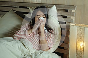 Young beautiful tired and ill Asian Japanese woman lying on bed at home sick suffering cold flu and temperature feeling unwell and