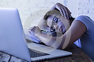 Young beautiful and tired student girl sleeping taking a nap lying on home laptop computer desk exhausted and wasted spending nigh photo