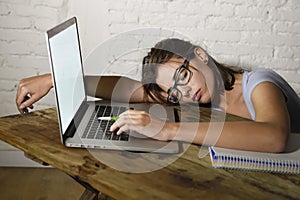 Young beautiful and tired student girl sleeping taking a nap lying on home laptop computer desk exhausted and wasted spending nigh photo