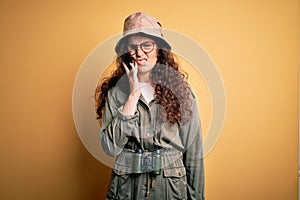 Young beautiful tourist woman on vacation wearing explorer hat and binoculars touching mouth with hand with painful expression