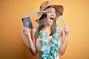 Young beautiful tourist woman on vacation wearing swimsuit and hawaiian lei holding passport pointing and showing with thumb up to