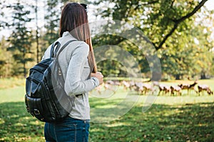 Young beautiful travel girl with backpack looking at wild reindeer grazing in the distance.