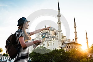 A young beautiful traveler girl in a hat with a backpack and a map next to the blue mosque is a famous sight in Istanbul