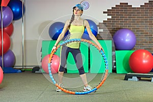 Young beautiful white girl in a yellow and gray sports suit does physical exercises with a hoop at the fitness center.