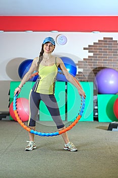 Young beautiful white girl in a yellow and gray sports suit does physical exercises with a hoop at the fitness center.