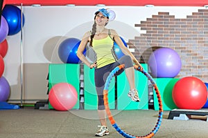 Young beautiful white girl in a yellow and gray sports suit does physical exercises with a hoop at the fitness center.