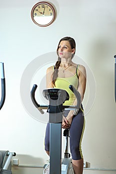 Young beautiful white girl in a yellow and gray sports suit is engaged on a stationary bike in the fitness club.