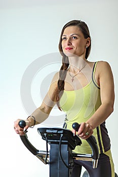 Young beautiful white girl in a yellow and gray sports suit is engaged on a stationary bike in the fitness club.