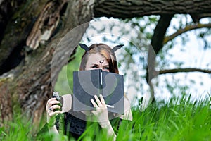 Young beautiful witch in black dress conducts a ceremony in a green forest on a summer day. Witchcraft