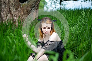 Young beautiful witch in black dress conducts a ceremony in a green forest on a summer day. Witchcraft