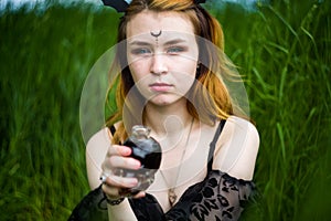 Young beautiful witch in black dress conducts a ceremony in a green forest on a summer day. Witchcraft