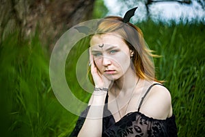 Young beautiful witch in black dress conducts a ceremony in a green forest on a summer day. Witchcraft