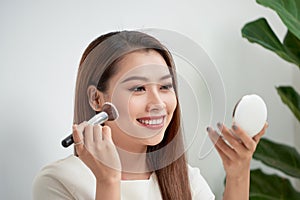 Young beautiful woman applying her make-up with a big brush , looking in a mirror