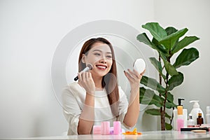 Young beautiful woman applying her make-up with a big brush , looking in a mirror